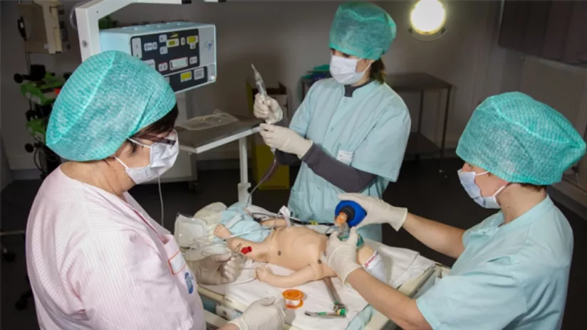 Photo de 2 étudiants et une professeure s'occupant d'un mannequin bébé pour s'entraîner