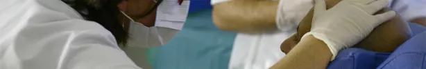 une médecin en blouse blanche et masque pose la main sur un patient pour un soin